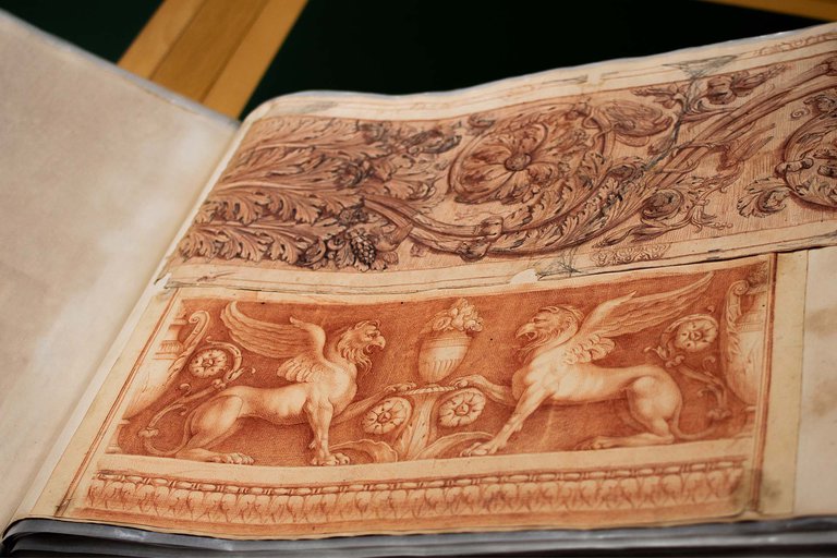 Geöffnetes Klebealbum auf der rechten Seite sind eingeklebte Zeichnungen zweier Friese zu sehen, eines mit Wellenranken, das andere mit einer Fruchtvase und zwei Greifen